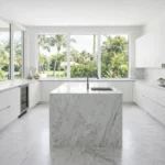 Kitchen Bright Palm Beach kitchen featuring sleek white cabinets, marble countertops and backsplash, integrated appliances, and expansive garden views.