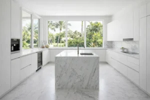 Bright Palm Beach kitchen featuring sleek white cabinets, marble countertops and backsplash, integrated appliances, and expansive garden views.